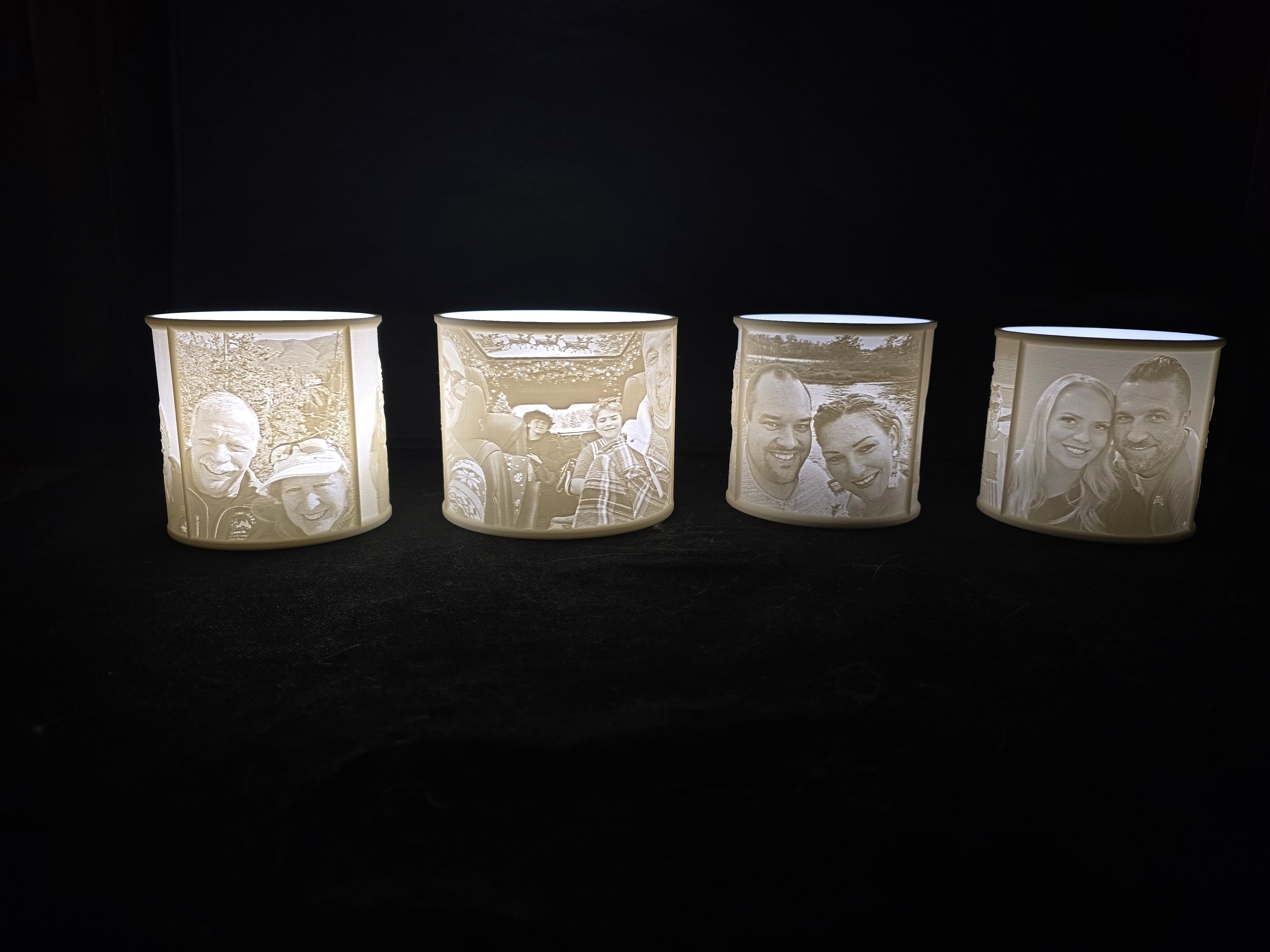 Four cylindrical candles with engraved faces on a black background