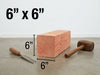 A 6x6 inch square wooden block shown on a gray floor against a white wall, with dimension lines and text indicating 6 inches on each side. A chisel and a wooden mallet are placed beside it.