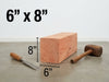 A 6 inch by 8 inch wooden block shown on a gray floor against a white wall, with dimension lines and text indicating its size. A chisel and mallet are placed beside it for scale.